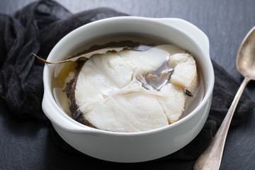 boiled fish with olive oil in dish on ceramic background