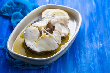 boiled fish with olive oil in dish on ceramic background