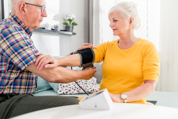 Senior husband doing blood pressure measurement to his wife at home