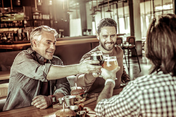 Positive delighted men touching glasses with beer