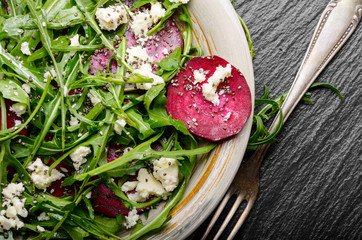 Top view at clay dish with beetroot arugula and feta cheese salad on slate stone tray closeup view....