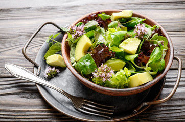 Clay dish with salad of avocado, green and violet lettuce, lamb's lettuce and oregano flowers with vintage fork aside
