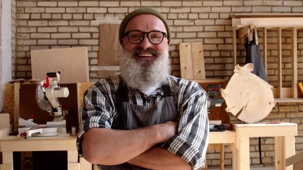 Medium shot of senior bearded handsome Caucasian craftsman looking at camera while crossing arms on his chest and laughing - Powered by Adobe