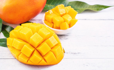 Beautiful chopped mango chunks with green leaves on bright white color timber background. Copy space, close up, macro. Tropical fruit concept.