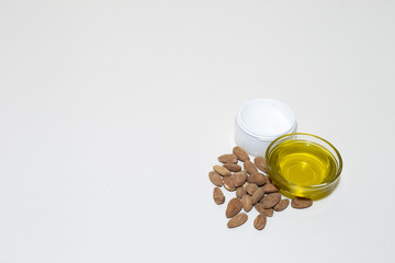 Almonds cream next to seeds used as ingredients and a small transparent glass bowl of oil – Beauty treatment for skin or face used in spa