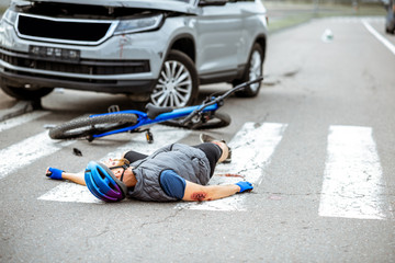 Scene of a road accident with injured cyclist lying on the pedestrian crossing near the broken bicycle and car