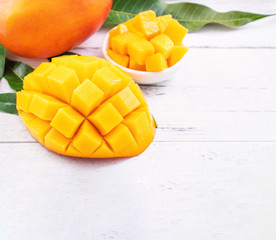 Beautiful chopped mango chunks with green leaves on bright white color timber background. Copy...