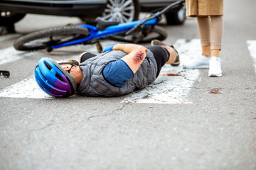 Road accident with injured cyclist lying on the pedestrian crossing near the broken bicycle and car driver on the background