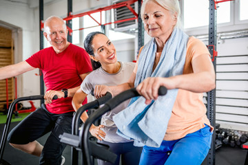 Fototapeta na wymiar Senior couple biking at the gym with personal trainer