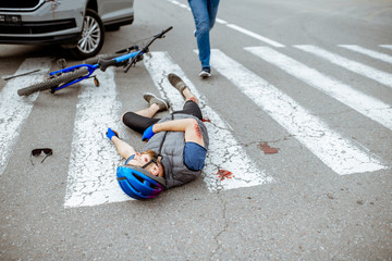 Road accident with injured cyclist lying on the pedestrian crossing near the broken bicycle and car...