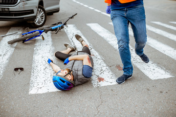 Road accident with injured cyclist lying on the pedestrian crossing near the broken bicycle and car driver running on the background