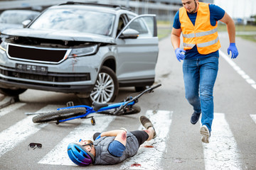Road accident with injured cyclist lying on the pedestrian crossing near the broken bicycle and car...