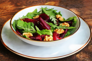 Healthy Beet Salad with fresh sweet baby spinach, arugula, nuts on wooden background