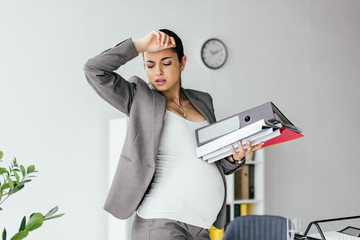 exhausted pregnant woman enduring pain and holding folders