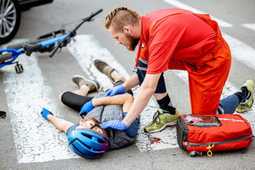 Medic applying first aid to the injured cyclist lying on the pedestrian crossing after the road...