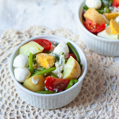 Two white bowls with light and healthy salad with tomato, eggs, green beans, mozzarella cheese and sauce. Delicious lunch for a couple
