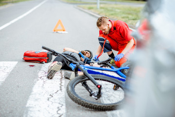 Medic applying first aid to the injured cyclist lying on the pedestrian crossing after the road accident, doctor measuring pressure © rh2010