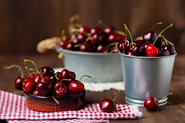 Composition with ripe cherries in metal bowls and clay brown plate. Vintage napkins as decor. Dacha style, countryside, cozy and cute, grandmother's kitchen
