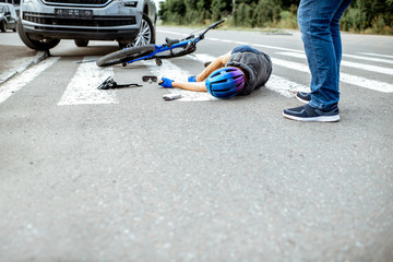 Scene of a road accident with injured cyclist lying on the pedestrian crossing near the broken bicycle and car