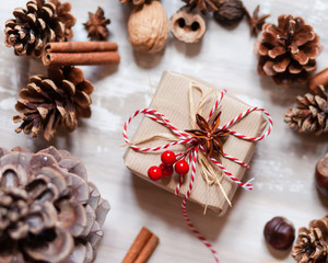 Composition with Christmas gift in hand made wrap. Rustic style, natural elements. Cones, craft paper, cinnamon, chestnut, walnut, anise, ropes, red berries serve to create holiday mood. Family time
