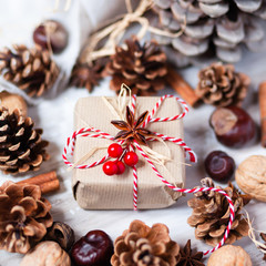 Composition with Christmas gift in hand made wrap. Rustic style, natural elements. Cones, craft paper, cinnamon, chestnut, walnut, anise, ropes, red berries serve to create holiday mood. Family time