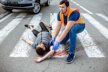 Man applying first aid to the injured bleeding person, wearing tourniquet on the arm after the road...