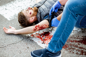 Applying first aid to the injured bleeding man, wearing tourniquet on the arm after the road...