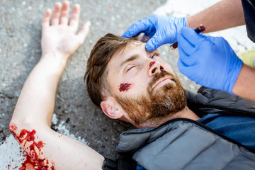 Medic checking unconscious person with flashlight, applying first aid to the bleeding person on the...