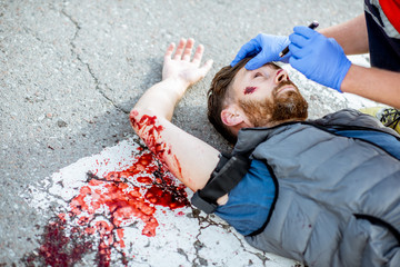 Medic checking unconscious person with flashlight, applying first aid to the bleeding person on the...