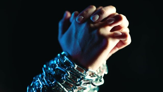 Female bound hands of slave chained with iron chain on black background. Slavery, prisoner, violence concept.