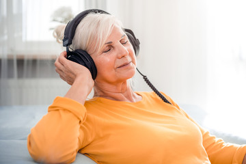 Relaxed senior woman listening her favourite music at home using big headphones