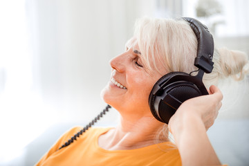 Relaxed senior woman listening her favourite music at home using big headphones