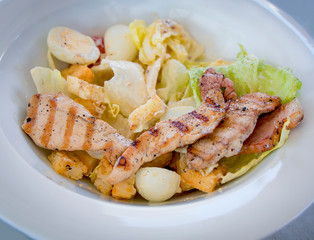 Caesar salad with chicken on a white plate in a cozy restaurant