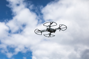 Quadrocopter against the blue sky with white clouds. The flight of the copter in the sky