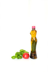 Transparent plastic bottle in the shape of a woman with a hat, with various spices and olive oil inside, one tomato and a basil sprig near, isolated