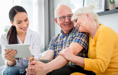 Nurse showing medical raport using tablet to senior couple at home