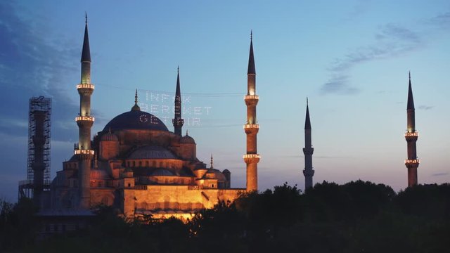 zoom in at dusk of the floodlit blue mosque exterior in istanbul, turkey- mahya says "infak bereket getirir" in english it means "help is bringing blessing".