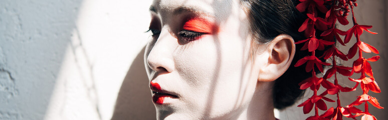 portrait of beautiful geisha with red and white makeup in sunlight with shadows, panoramic shot