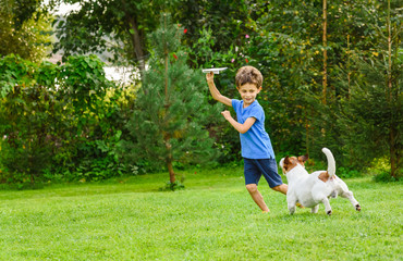 Kid playing with paper airplane and dog outdoors at backyard lawn