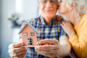 New house concept, happy senior couple holding small home model