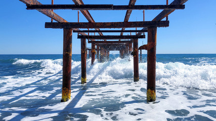 View of the breaking wave of a rusty metal pier. Seascape on a sunny day. 