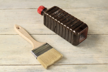A brush lies next to a plastic bottle with stain on an old white vintage wooden plank table. Place for text or logo.