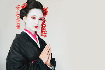 smiling beautiful geisha in black kimono with greeting hands isolated on white with copy space