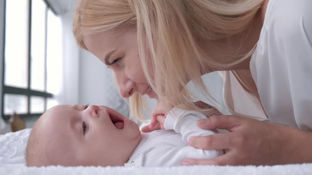 mother love, young parent gently touches and kisses her adorable baby girl who lies on the changing table