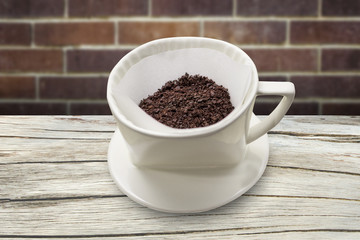 cup of drip coffee with paper filter tool on wood table and brick wall