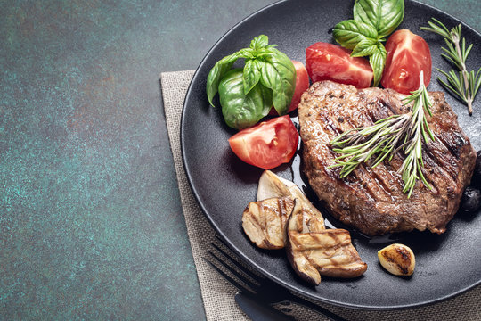 Grilled beef steak with mushrooms and vegetables on black plate, with copy space