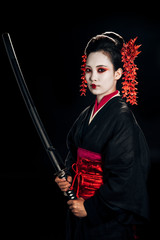 beautiful geisha in black kimono with red flowers in hair holding sharp katana isolated on black