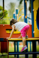 Fototapeta premium Adorable little 1-2 year old Asian toddler girl having fun on playground. View from behind toddler trying to climb the stairs.