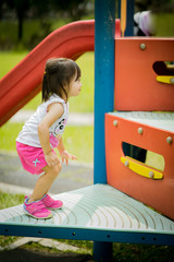 Fototapeta na wymiar Adorable little 1-2 year old Asian toddler girl having fun on playground. View from side.