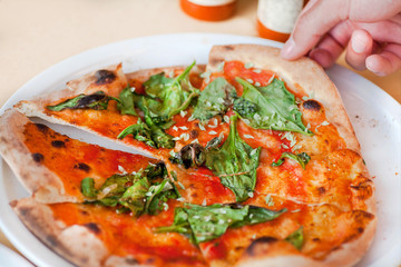 Taking slice of hot pizza. Tasty pizza with with cheese and greens, closeup view. Hand taking italian food